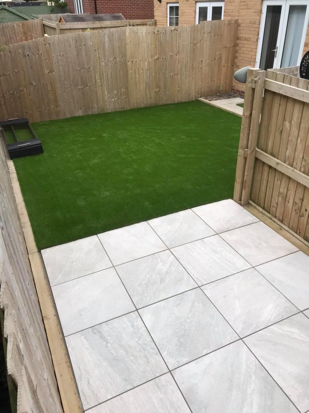 Small fenced garden with artificial lawn and square paving slabs